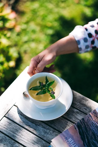 Aurora, Ihr Hotel in Lech am Arlberg Hand hält Tasse mit Kräutertee auf Holztisch im Garten
