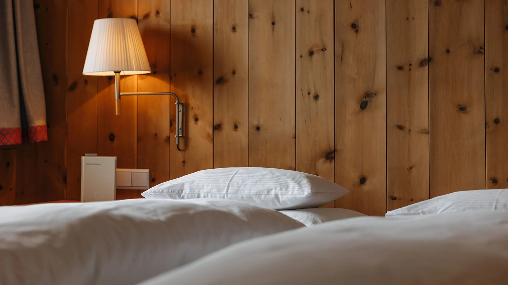 Aurora, Ihr Hotel in Lech am Arlberg Weißes Bett mit Kopfkissen und Wandlampe an Holzwand
