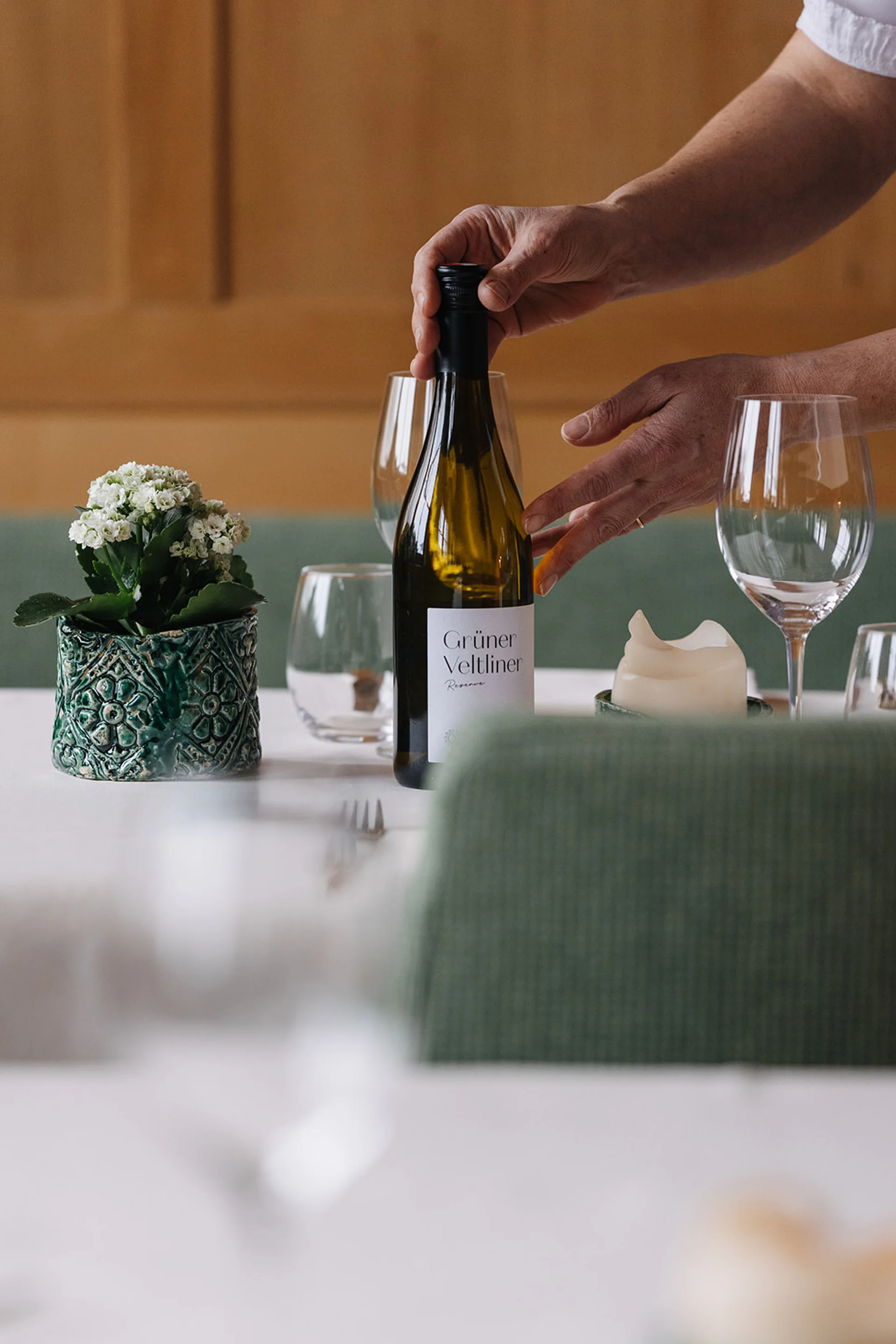 Aurora, Ihr Hotel in Lech am Arlberg Person stellt Weinflasche Grüner Veltliner auf gedeckten Tisch mit Gläsern
