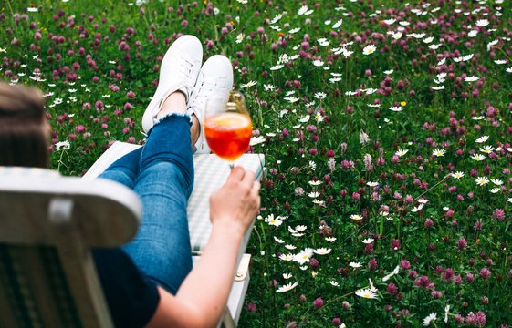 Mann liegt im Liegestuhl in einer Wiese mit einem Drink in der Hand.