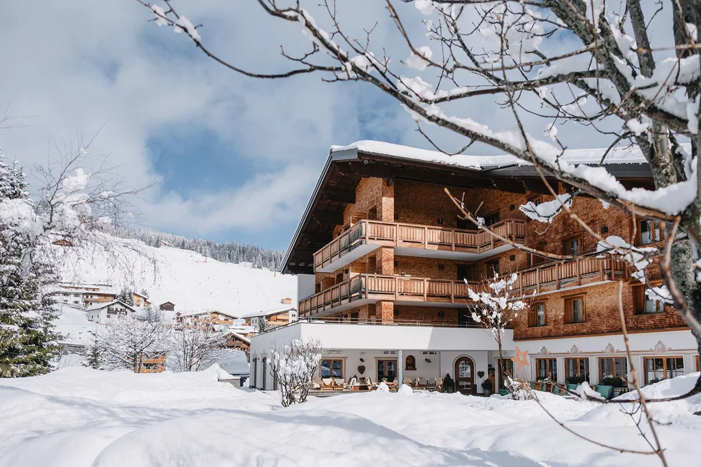 Aurora, Ihr Hotel in Lech am Arlberg Verschneites Hotelgebäude mit Balkon in einer winterlichen Alpenlandschaft