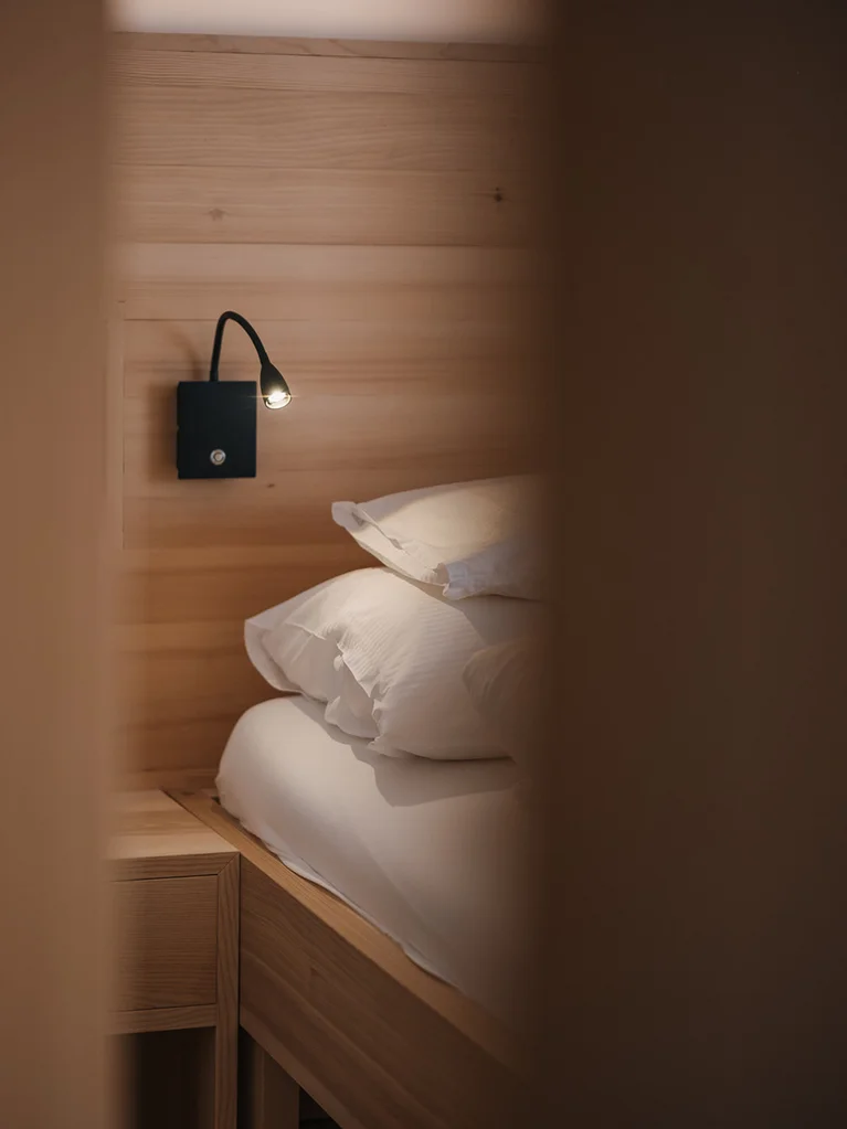 Aurora, Ihr Hotel in Lech am Arlberg Gemütliches Bett mit Leselampe an Holzwand