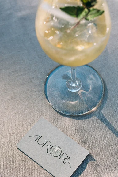 Aurora, Ihr Hotel in Lech am Arlberg Cocktailglas mit einer Minze und eine Visitenkarte mit dem Logo Aurora