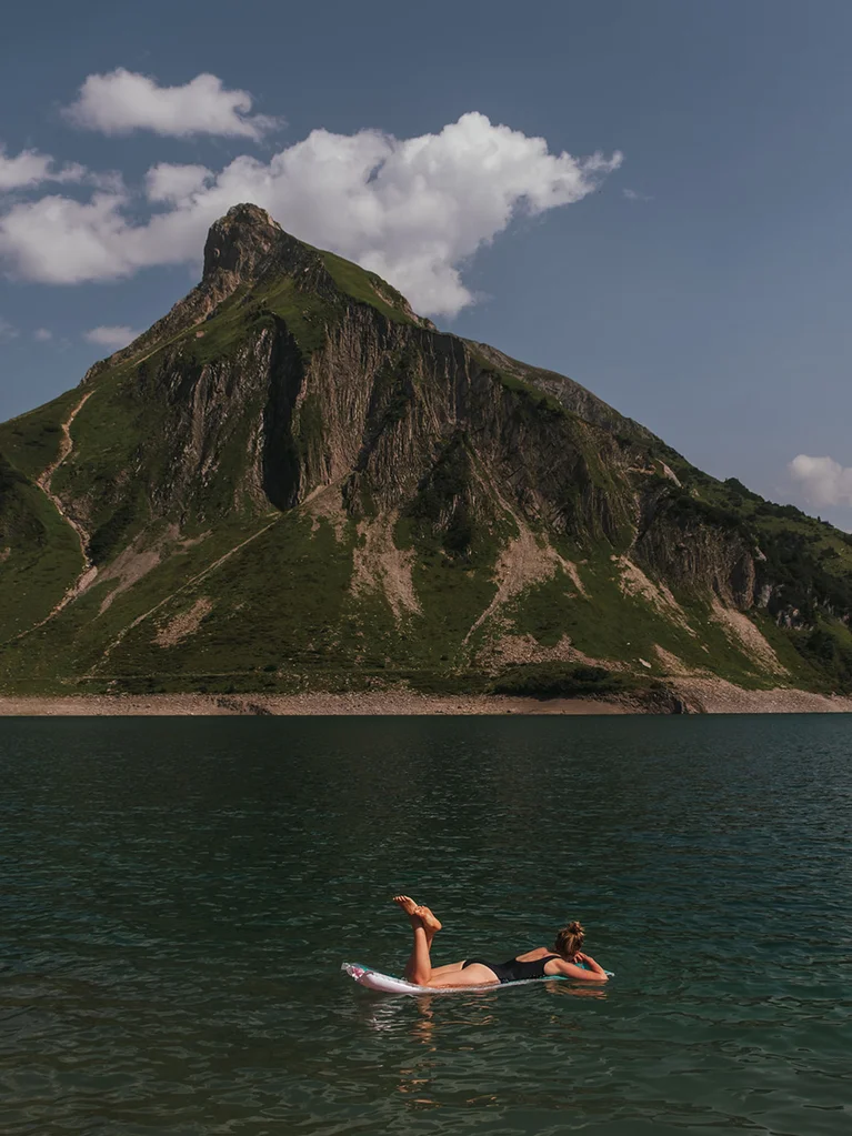 Culture and events in Lech am Arlberg Woman relaxing floating on water with mountain backdrop under cloudy sky