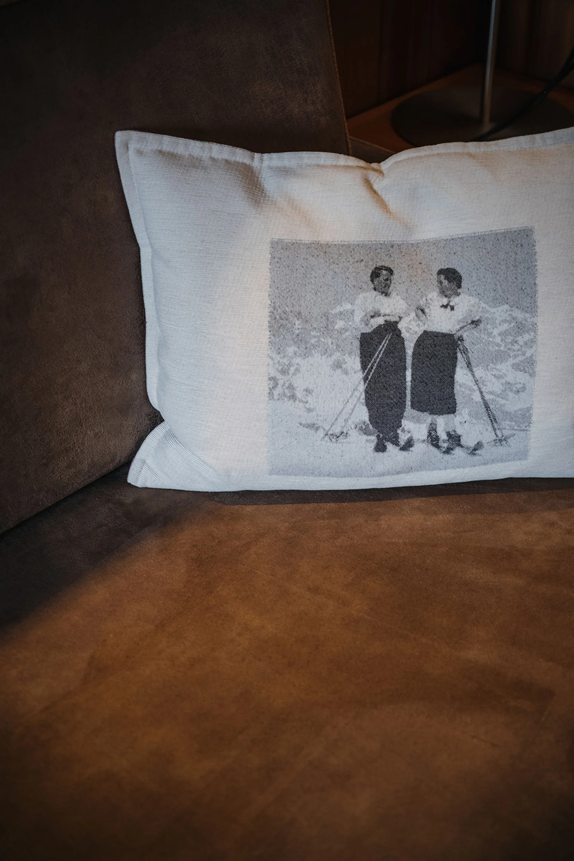 Aurora, Ihr Hotel in Lech am Arlberg Kissen mit Bild von zwei Frauen in altertümlicher Kleidung auf braunem Sofa